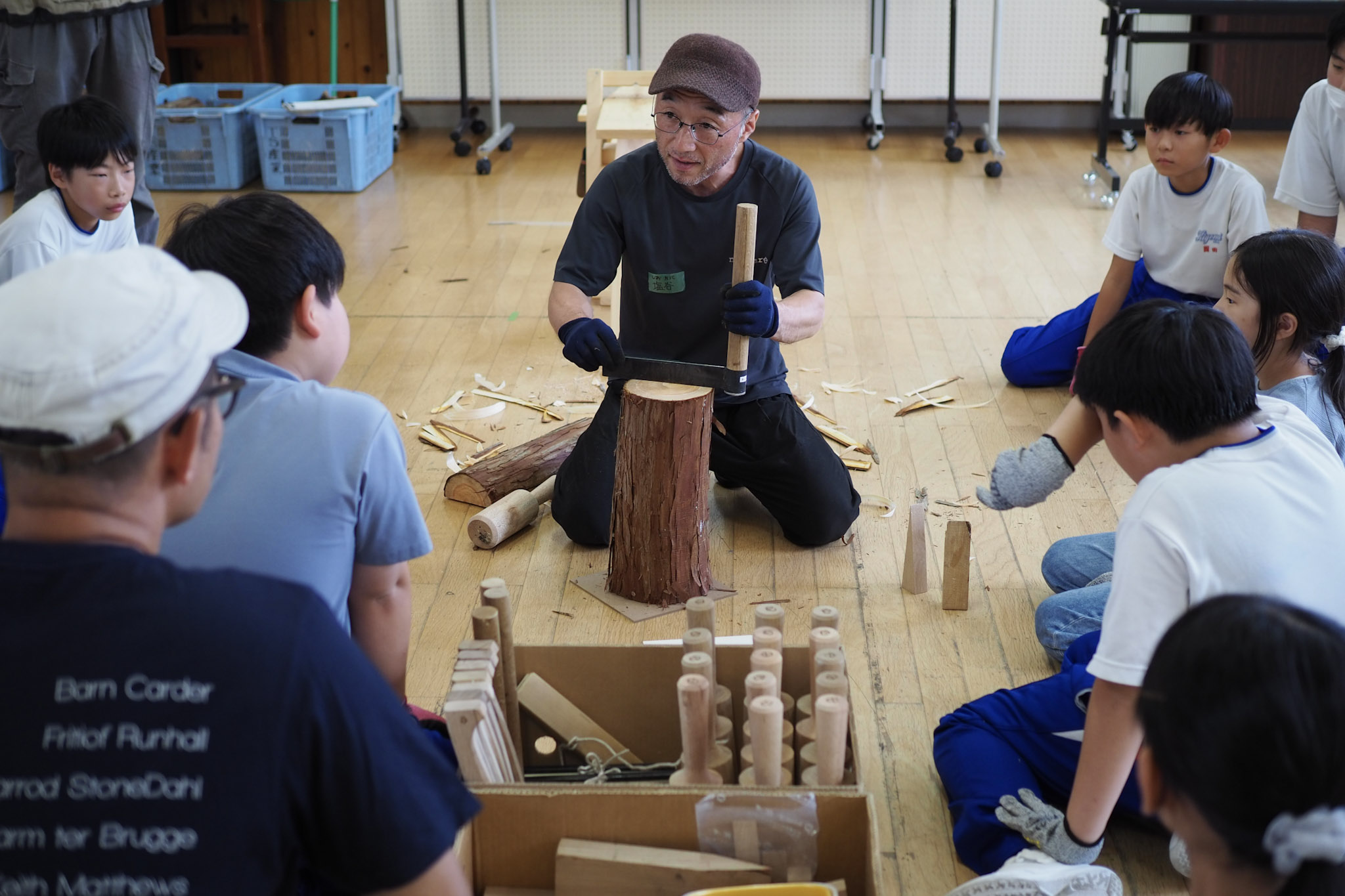 マンリキの使い方を説明するのは、地元・清見町で木工所を営む塩谷さん(写真中央)。座面となるヒノキは塩谷さんが間伐したもの。授業で児童が間伐したヒノキはスツールの脚として活用。